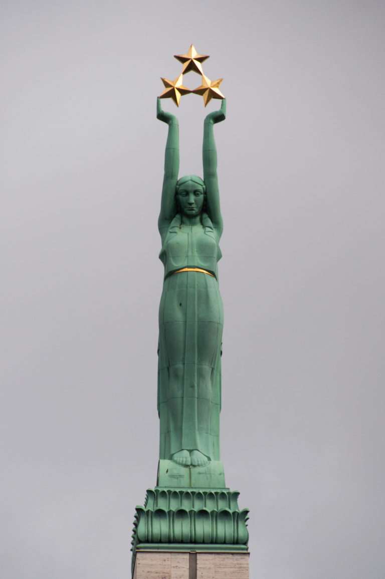 Full upper figure of Liberty on the Freedom Monument, raising three gilded stars above a green pedestal.