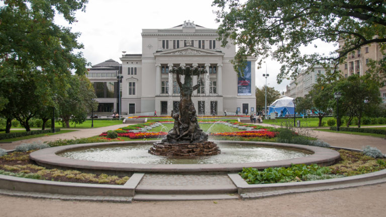 Circular Nymph Fountain basin centered in landscaped gardens with the Latvian National Opera beyond.