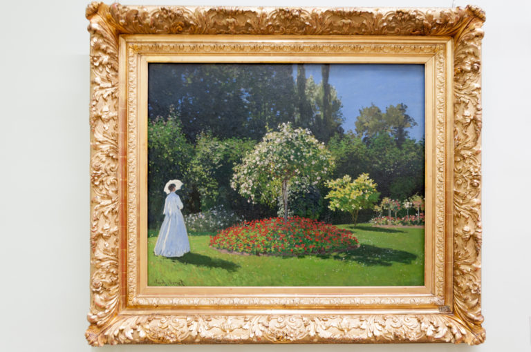 Claude Monet’s Lady in a Garden, with Jeanne-Marguerite Lecadre in white standing beside vivid flower beds and dense greenery.