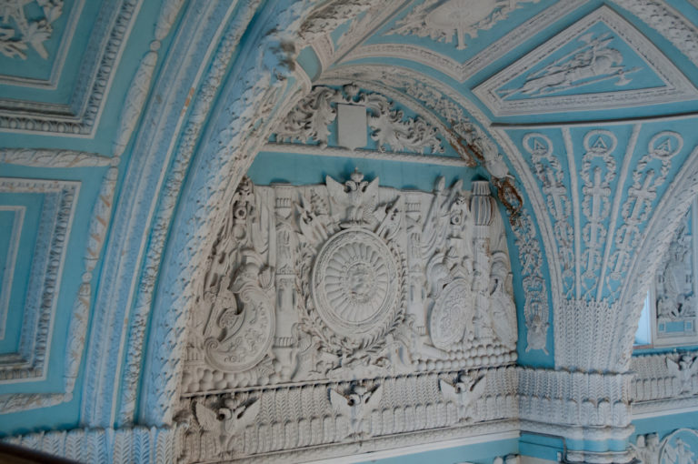 Close view of a pale blue and white palace arch covered with classical reliefs, rosettes, and ornamental stucco.