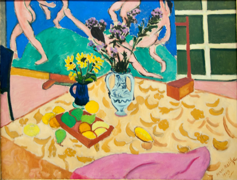 Henri Matisse’s 1909 Still Life with ‘Dance’, with fruit and flower vases on a patterned table before cropped dancing figures and a green window grid.