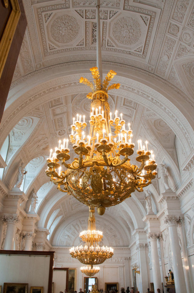 Long white neoclassical gallery with ornate vaulted ceiling and a row of large gilded chandeliers.