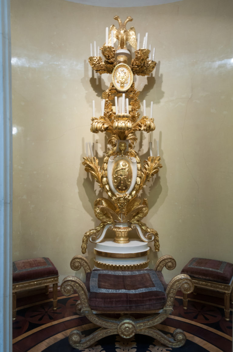 Frontal view of an elaborate gilded clock with circular dials, scrolling ornament, and sculptural base on a console.