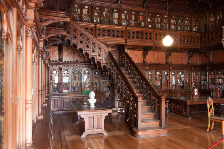 Gothic Library of Nicholas II with dark carved bookcases, upper gallery, wooden staircase, central table, portrait bust, and reading lamp.