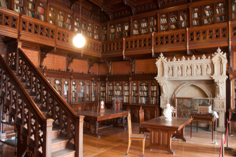 Nicholas II’s Gothic Library with dark oak bookcases and gallery surrounding a pale carved Gothic fireplace, wooden tables, and portrait bust.