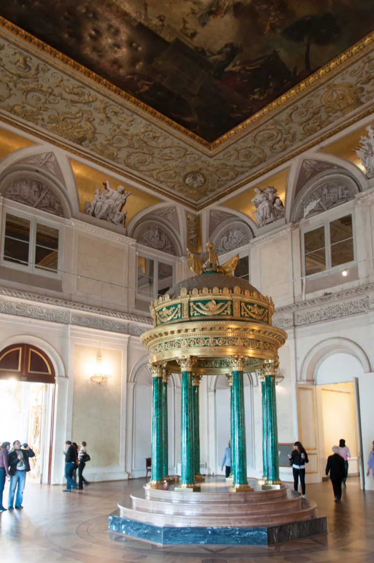 Malachite Rotunda with polished green columns and gilded domed crown standing in a pale Winter Palace hall beneath a painted ceiling.
