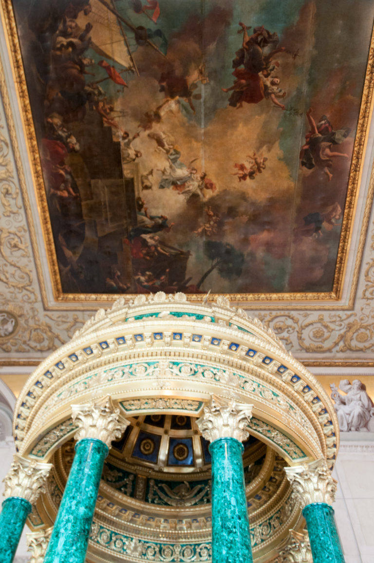 Upward view past green columns and ornate circular pavilion crown toward a large painted ceiling panel in the Hermitage.