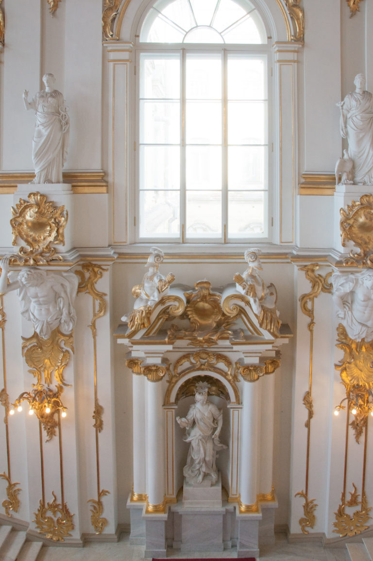 Jordan Staircase wall detail with arched window, ornate sculptural niche, broken gilded pediment, relief decoration, and flanking statues.