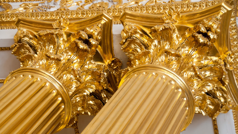 Close-up of paired gilded leafy capitals above fluted columns in the Winter Palace’s Armorial Hall.