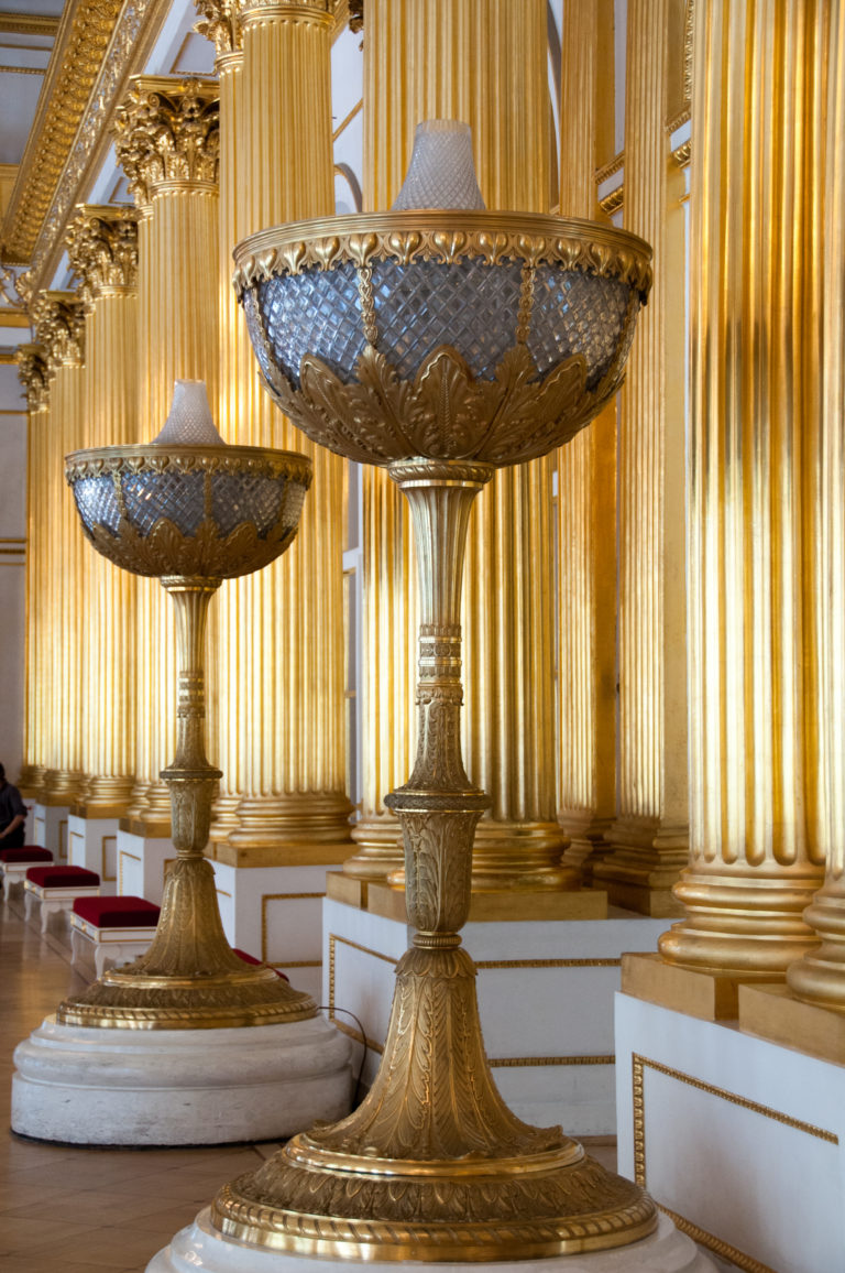 Pair of monumental pedestal bowls with dark basins and gilded mounts standing beside the gilded columns of the Armorial Hall.
