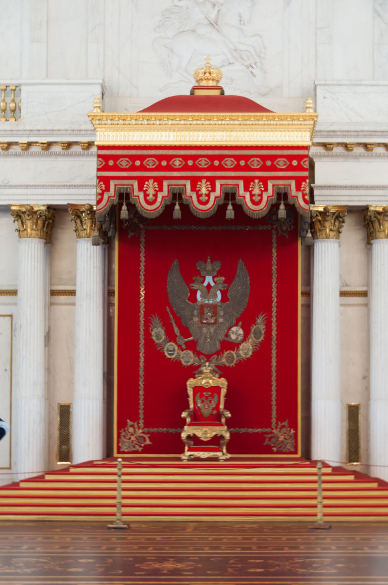 Centered imperial throne beneath red canopy with double-headed eagle, white columns, gilded emblems, and red-carpeted steps.