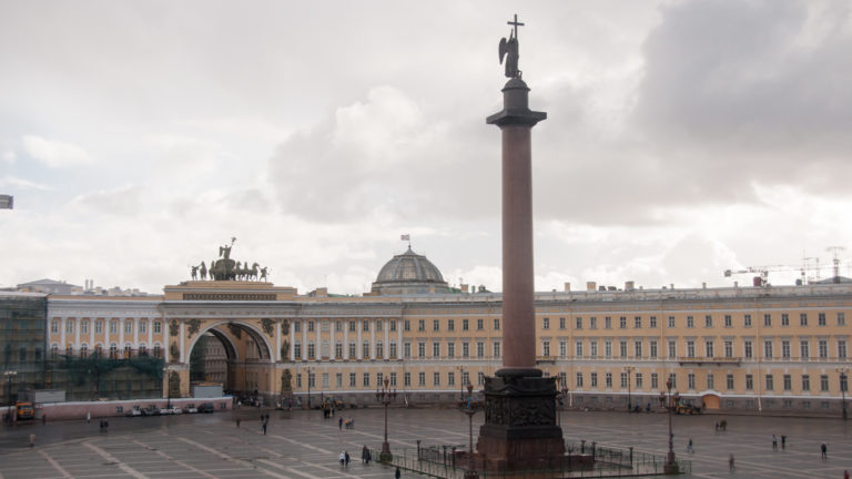Alexander Column centered on Palace Square before the General Staff Building, triumphal arch, and rooftop sculpture.