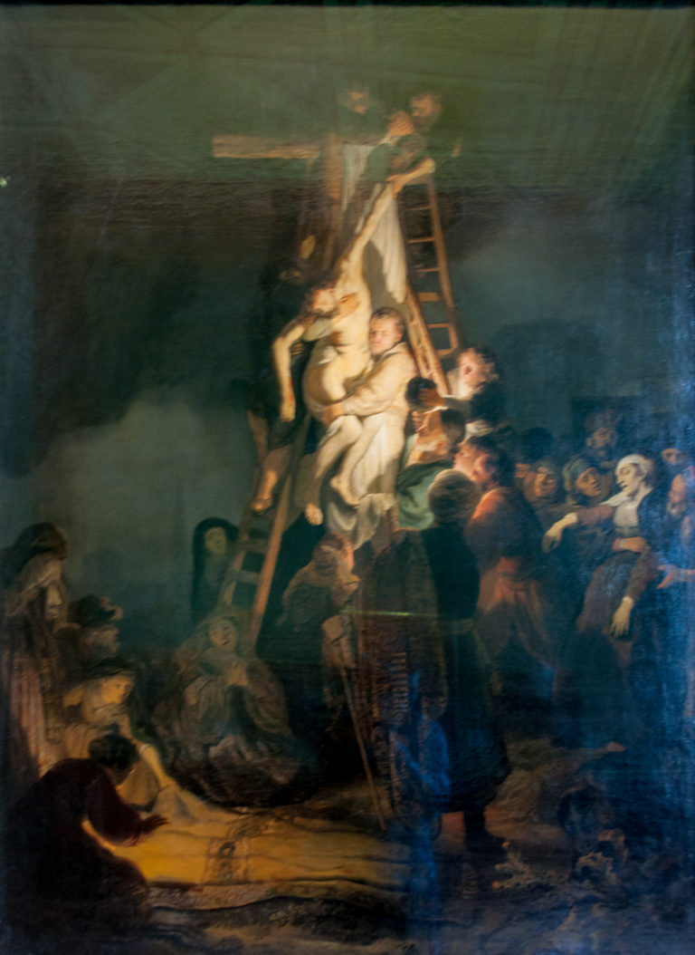 Dark biblical painting of figures lowering Christ beside a ladder, with concentrated light on the central group and deep surrounding shadow.