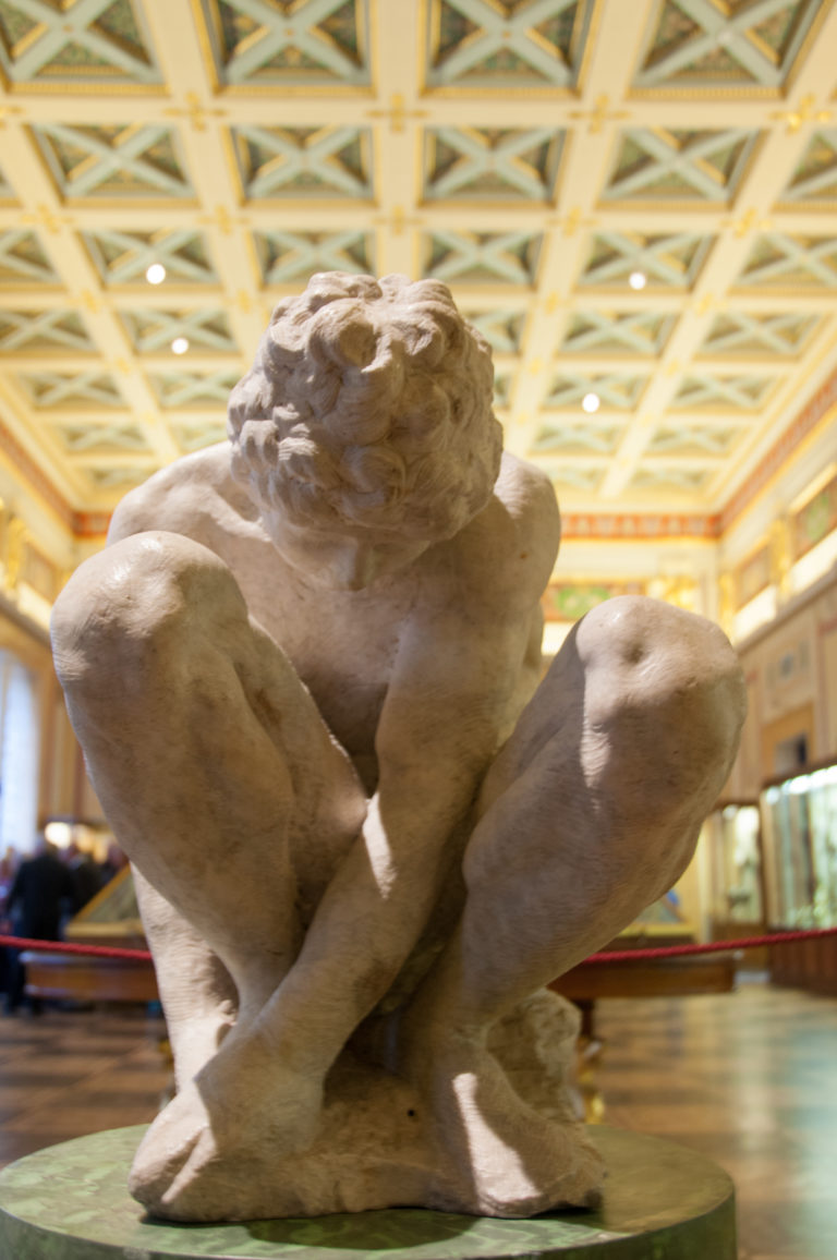 Michelangelo’s unfinished marble Crouching Boy, a nude youth folded tightly forward with bent limbs and lowered head.