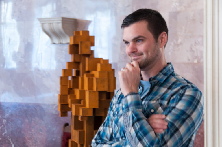 Close portrait of a visitor beside the upper section of a stacked-block figurative sculpture in a pale marble gallery.