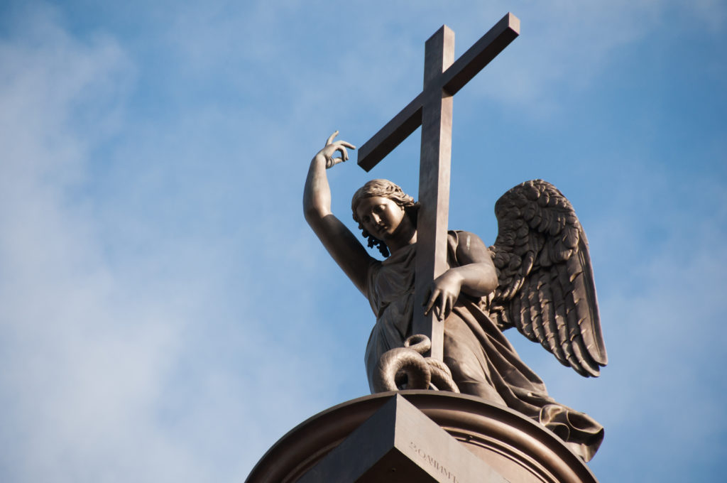 Close low-angle view of the winged angel and tall cross crowning the Alexander Column against a blue and cloudy sky.