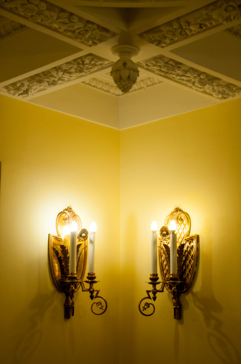 Two matching illuminated wall sconces with lattice-like backplates and candle-form lamps on a yellow wall.