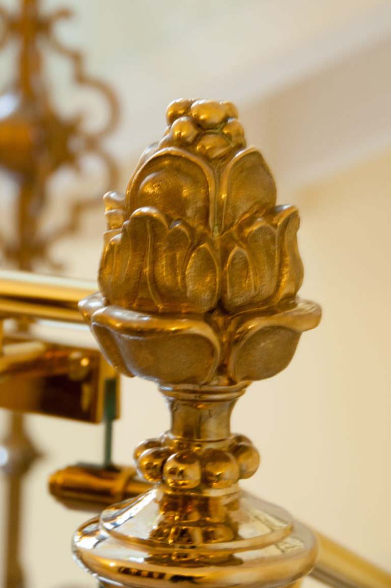 Close-up of a gilded floral finial mounted on a polished interior rail, with the background out of focus.