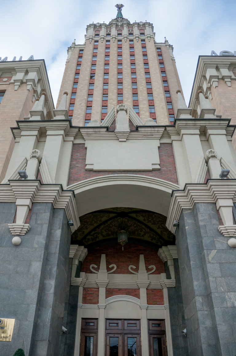 Low-angle view of Hotel National Moscow entrance façade with dark stone piers, arched portal, and tall windowed upper stories.