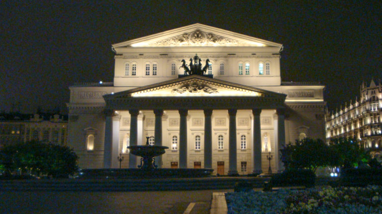 Illuminated Bolshoi Theatre at night, with its columned portico, triangular pediment, and quadriga above the façade.