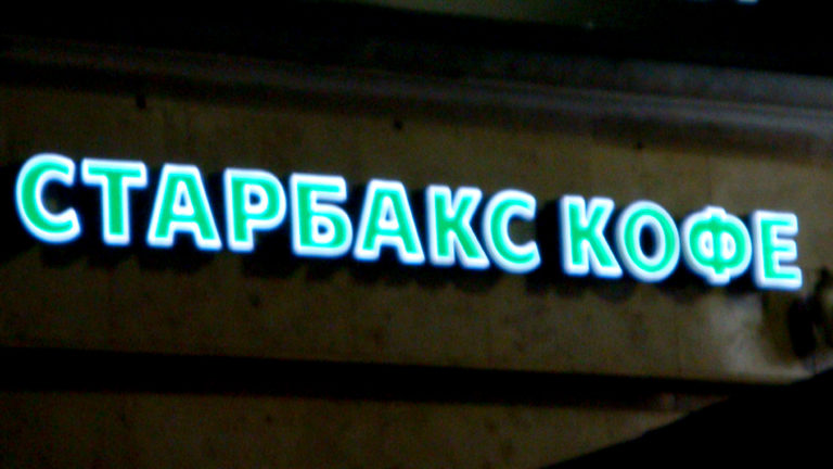 Illuminated Cyrillic sign reading 'СТАРБАКС КОФЕ' against a dark storefront at night.