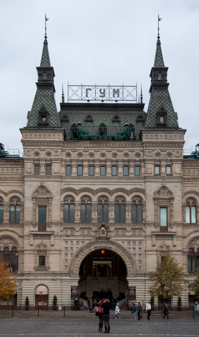 Frontal view of GUM's ornate stone façade and central arched entrance, with Cyrillic GUM letters along the roofline.