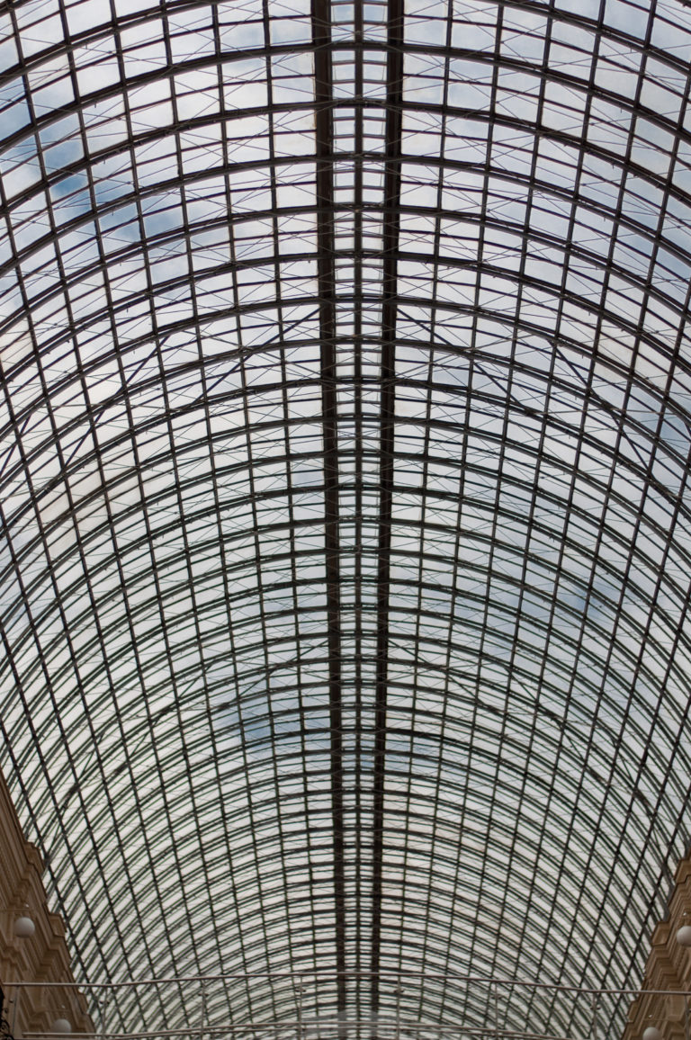 Close upward view of GUM's curved iron-and-glass roof, filled with repeating metal ribs and rectangular glazing panels.