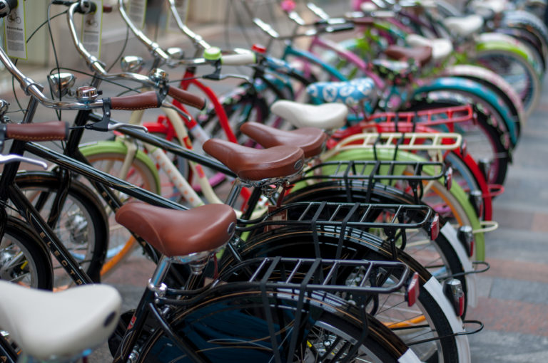 Close diagonal row of parked bicycles with brown saddles, rear racks, and colorful frames fading into soft focus.