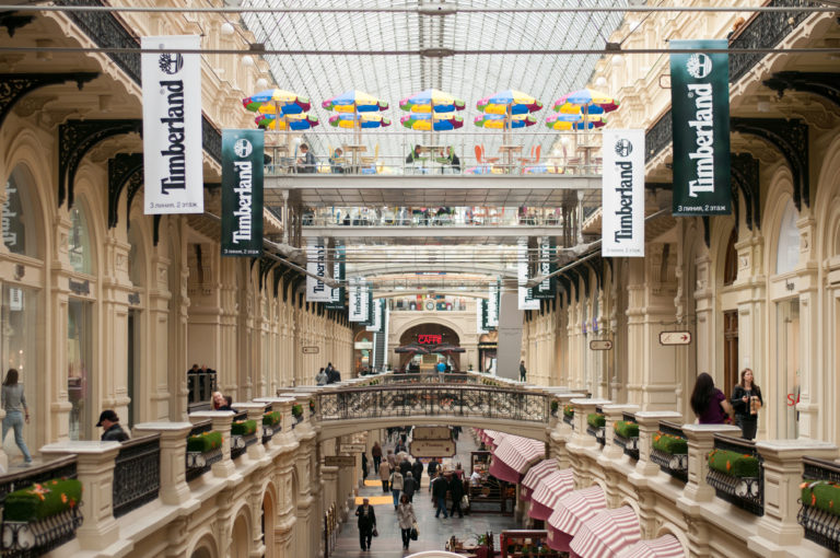 Long view down GUM's interior arcade with hanging banners, bridges, striped awnings, and shoppers below.