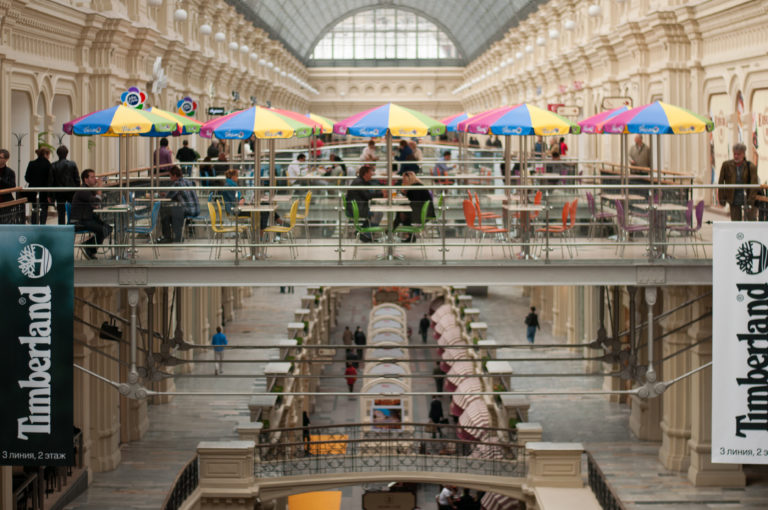 Colorful café umbrellas on an upper level of GUM above the multi-story shopping arcade and cream architectural galleries.