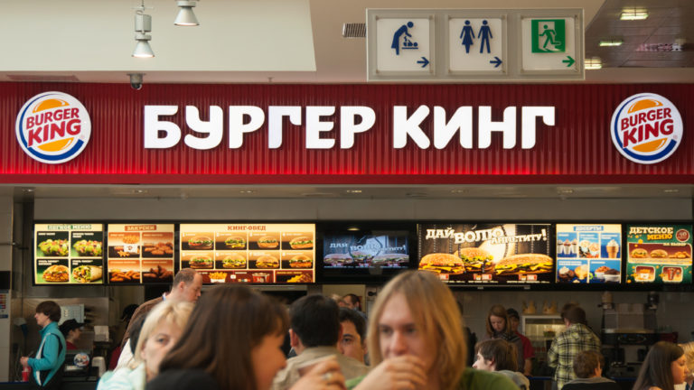 Customers at a Burger King counter beneath large Cyrillic Burger King signage and illuminated menu boards.