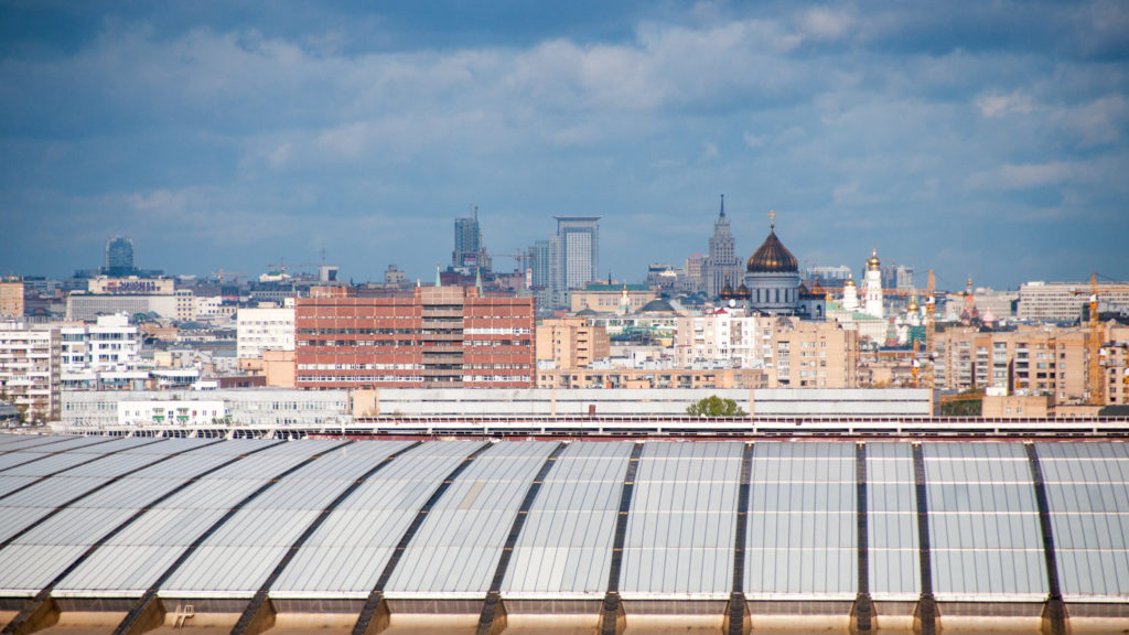 Moscow skyline beyond a broad glass roof, with the golden-domed Cathedral of Christ the Saviour near the center.