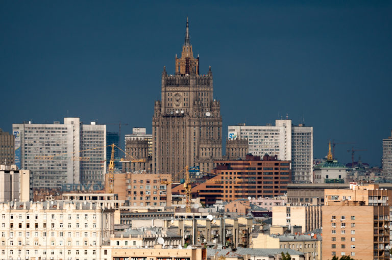 Ministry of Foreign Affairs Stalinist skyscraper rising above dense Moscow buildings against a dark blue-gray sky.