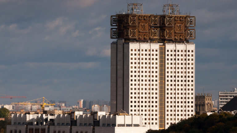Russian Academy of Sciences Presidium building with broad white tower and elaborate golden-brown rooftop crown under dark clouds.