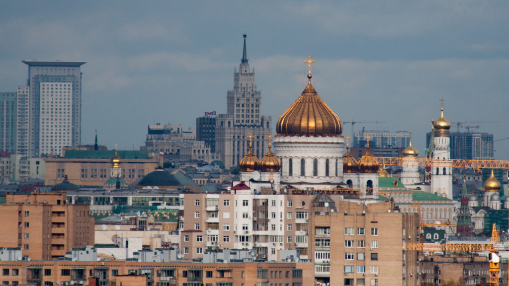 Gold domes of the Cathedral of Christ the Saviour among city buildings with a Stalinist high-rise in the distance.