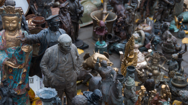 Crowded Moscow market display of metal figurines, small sculptures, candlesticks, and decorative objects.