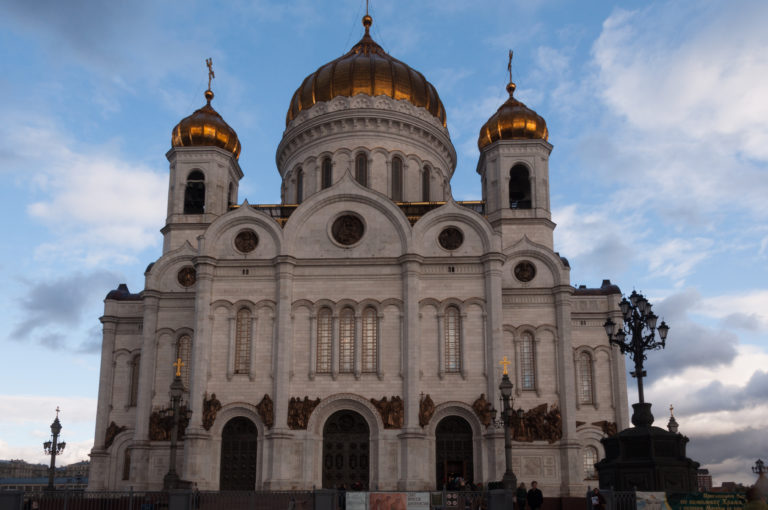 Low frontal view of the Cathedral of Christ the Saviour with white arched façade, reliefs, and large gilded dome.