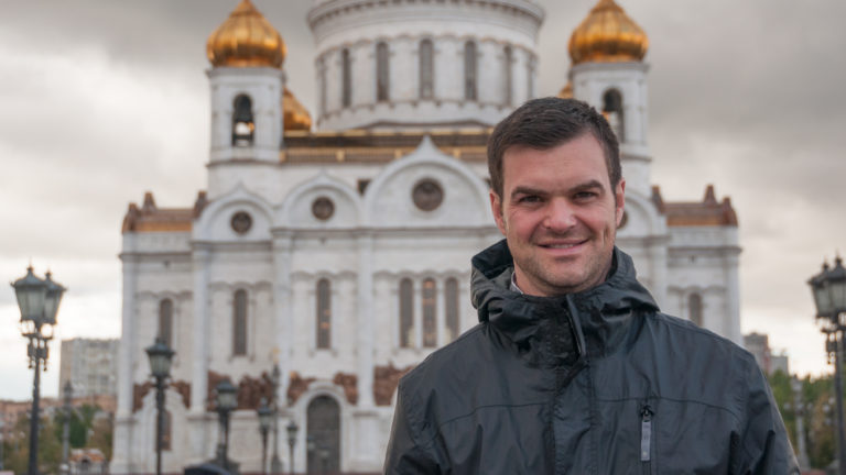 Man in a dark jacket smiling in front of the softly focused Cathedral of Christ the Saviour.