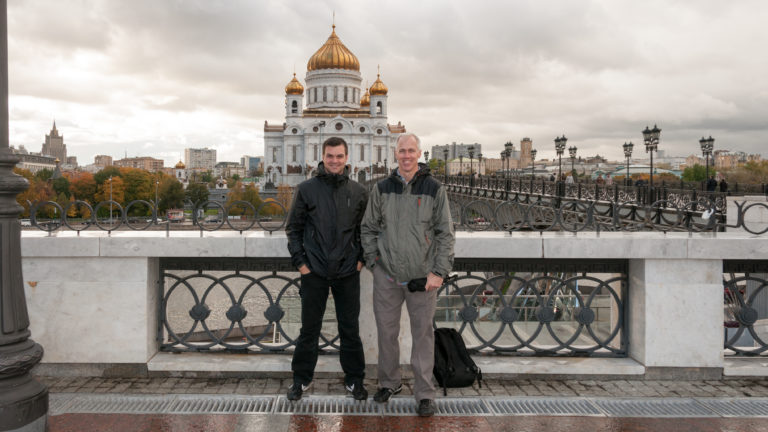 Full-length portrait of two men on Patriarshy Bridge with the Cathedral of Christ the Saviour behind them.