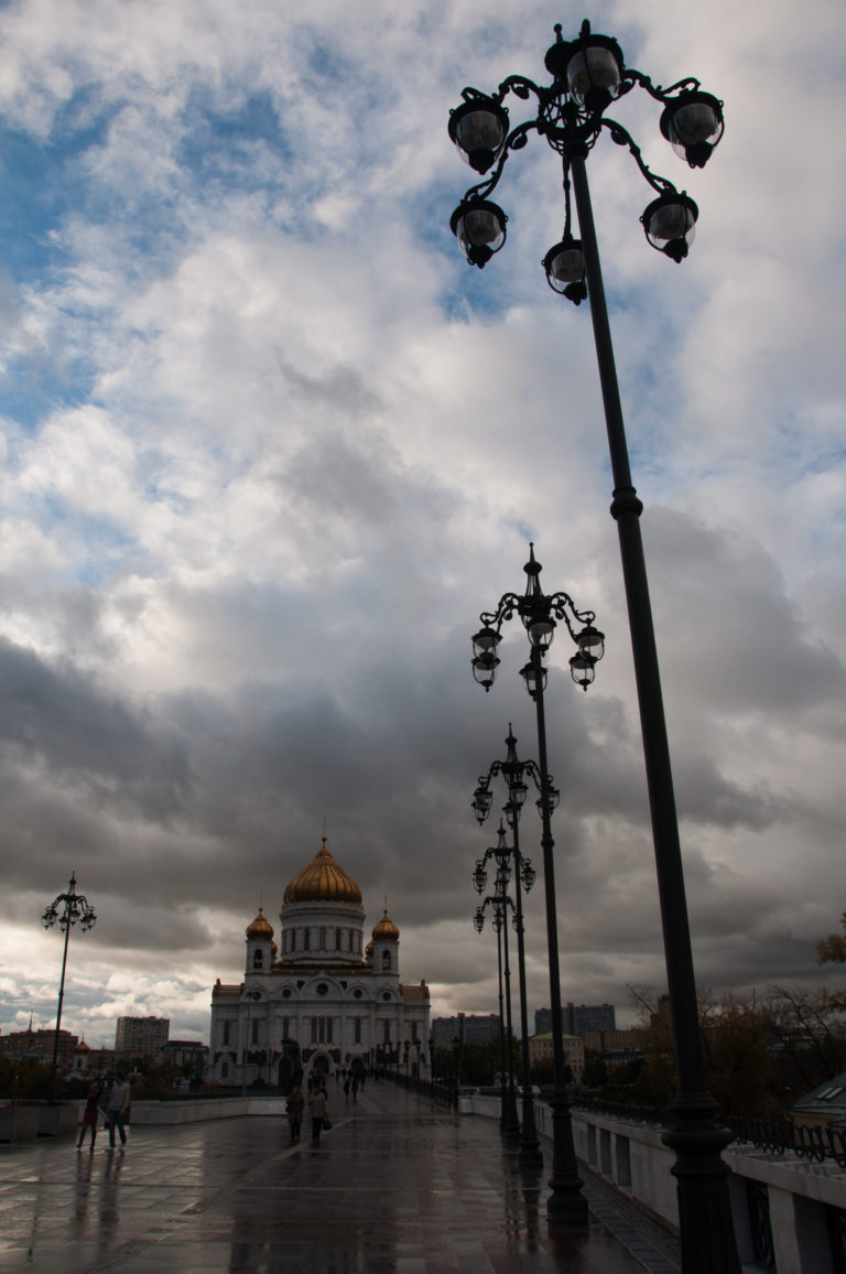 Cathedral of Christ the Saviour at the end of a bridge lined with ornate black streetlamps under dark clouds.