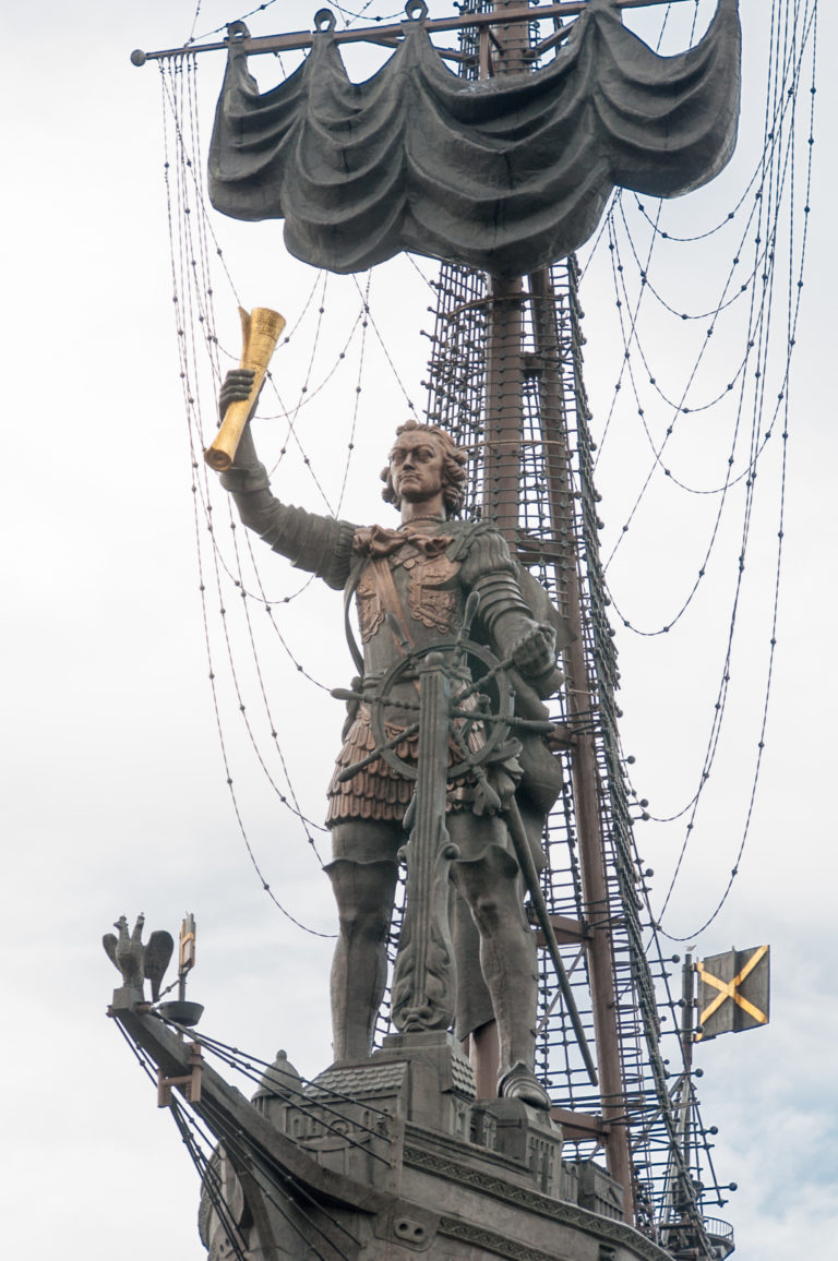 Close view of Peter I holding a golden scroll amid the masts, sails, and rigging of his Moscow monument.