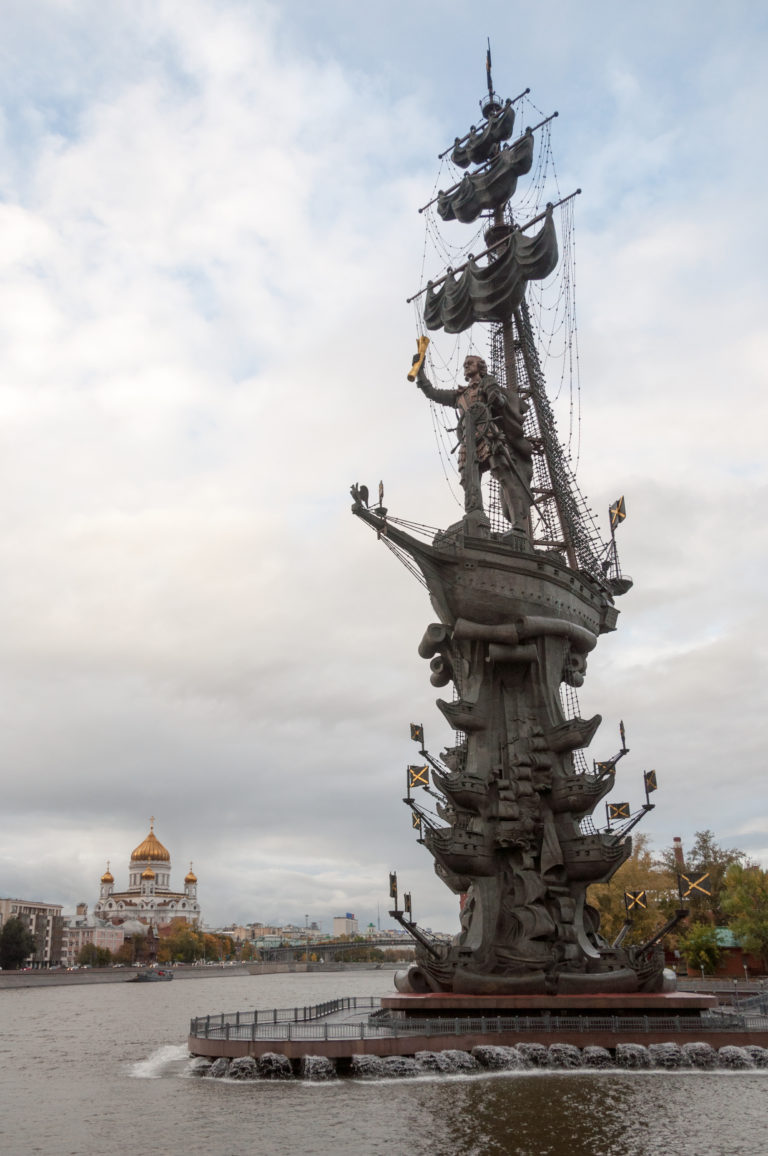 Peter the Great Monument rising from a ship-shaped base in the Moscow River beneath a cloudy sky.