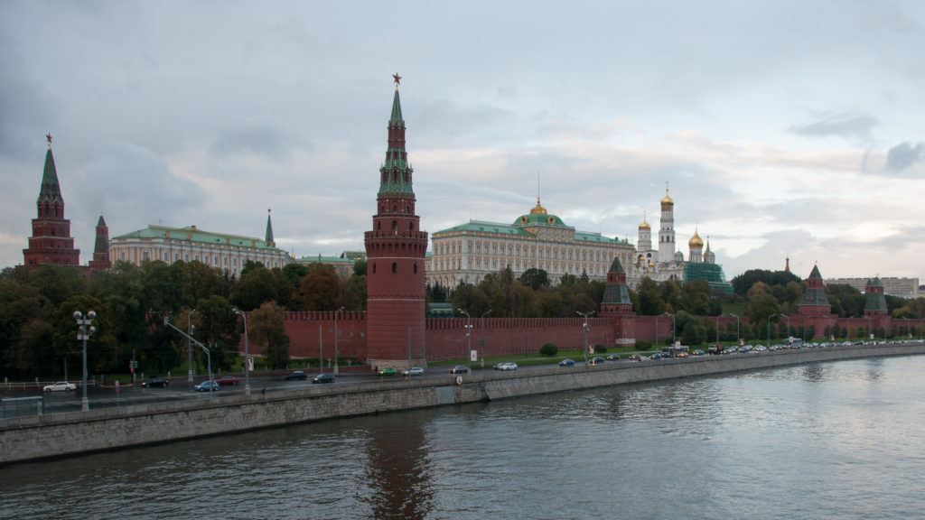 Moscow Kremlin's red walls and towers beside the Moskva River, with palace buildings and gilded domes behind.