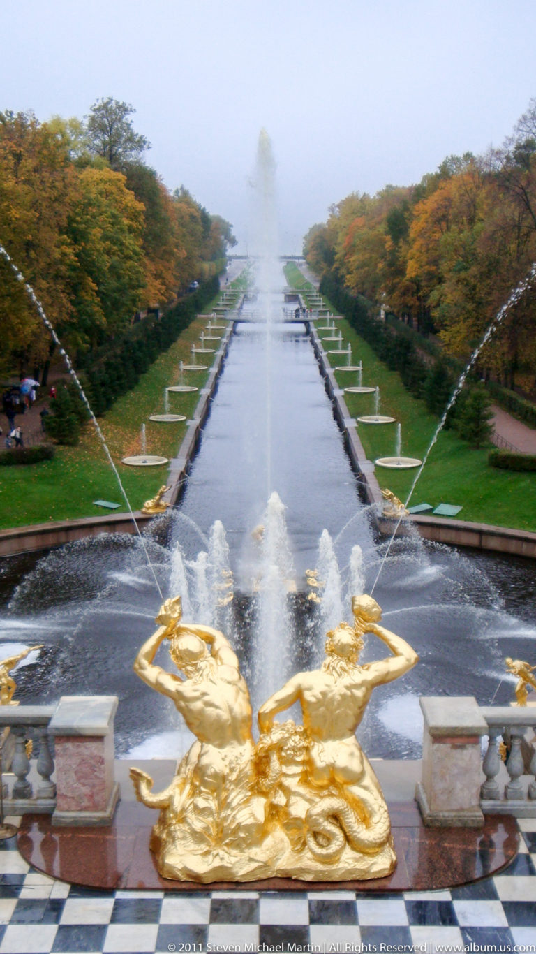 Long Sea Channel lined with fountains and autumn trees, viewed past gilded figures at Peterhof.