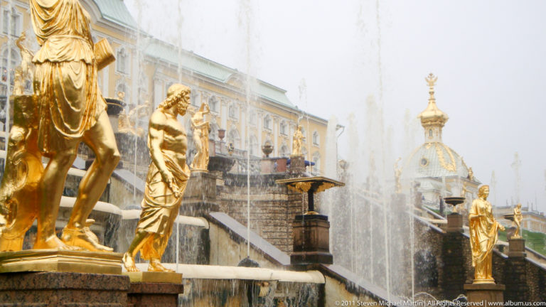 Close view of gilded figures, fountain spray, cascade masonry, and palace architecture at Peterhof.