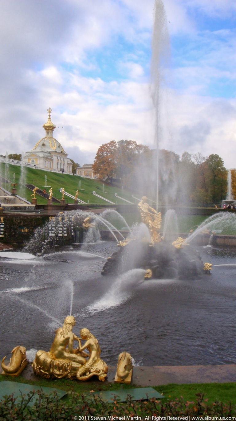 Large vertical fountain plume with gilded sculptures and lower jets before landscaped Peterhof terraces.