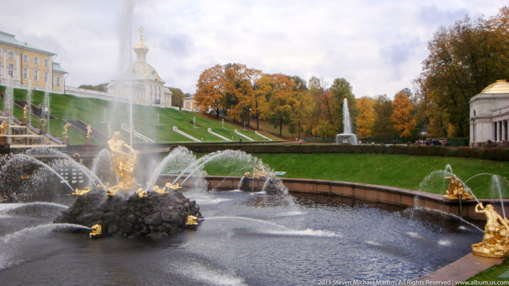 Grand Cascade basin with gilded figures, fountain jets, grassy slope, and a domed pavilion at Peterhof.
