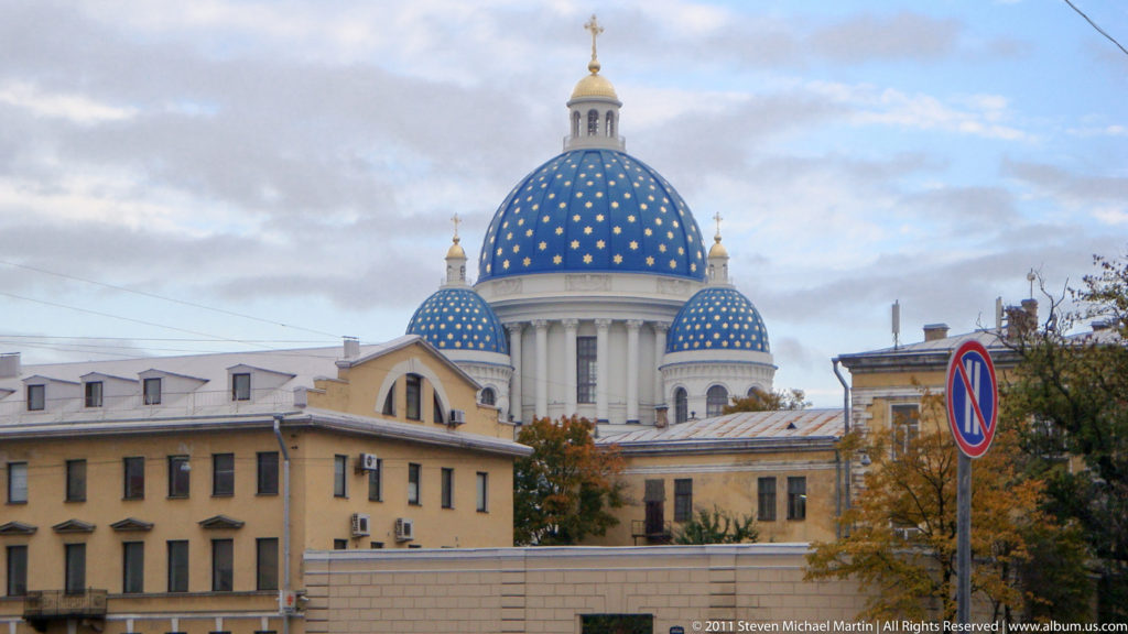 Large blue dome with gold stars and smaller matching domes rising above pale city buildings.