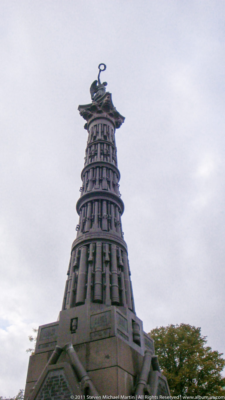 Low-angle view of a dark tiered monument with vertical ribs and a sculptural finial.