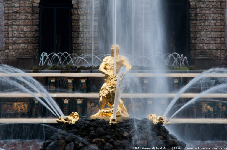 Gilded Samson figure over a lion amid high spray and arcing jets before dark cascade arches.